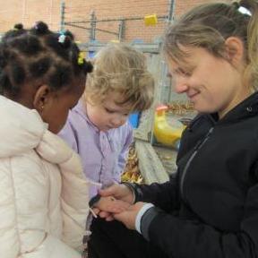 Two toddlers intently examining a bug with a Global Early Childhood Educator